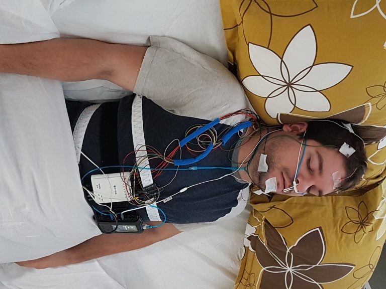 Une personne dort équipée d'un casque d'électroencéphalographie pendant une étude de polysomnographie, illustration de la mesure EEG du sommeil